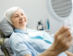 An older lady smiling in the mirror while in the dentist chair