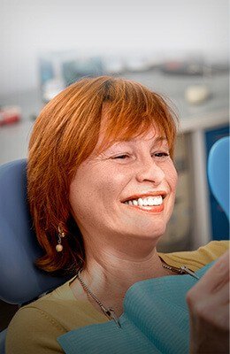 Older woman with orange hair seeing her smile in mirror in dental chair