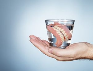 Outstretched hand holding a glass of water with dentures 