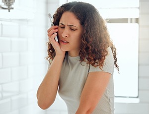 a woman holding her mouth in pain after brushing her teeth