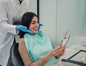 a woman looking in a mirror after receiving a dental cleaning