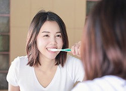 Woman brushing her teeth while looking in the mirror