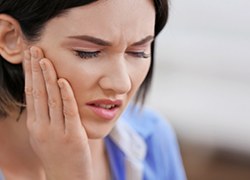 Woman with hand on cheek who is experiencing dental pain