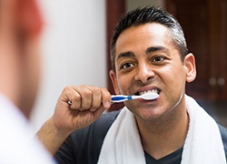 Man with greying hair looking in the mirror while brushing his teeth