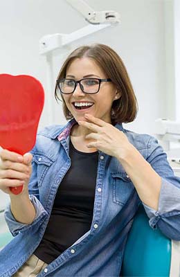 Young woman seeing her smile in a mirror in dental chair