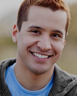 Young man in gray hoodie grinning outdoors