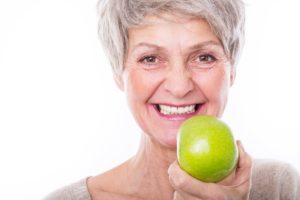 Older woman with dental implants in Carrollton holding an apple.