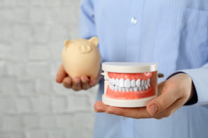 a patient holding a piggy bank and a model of dentures